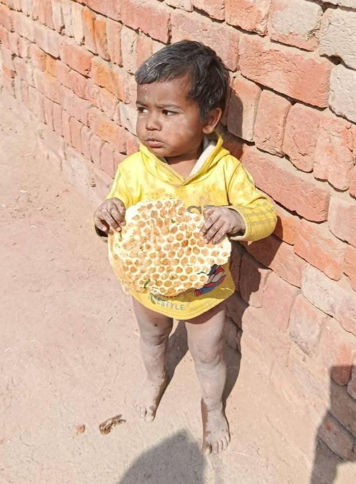 A toddler alone against a brick wall, holding a flatbread