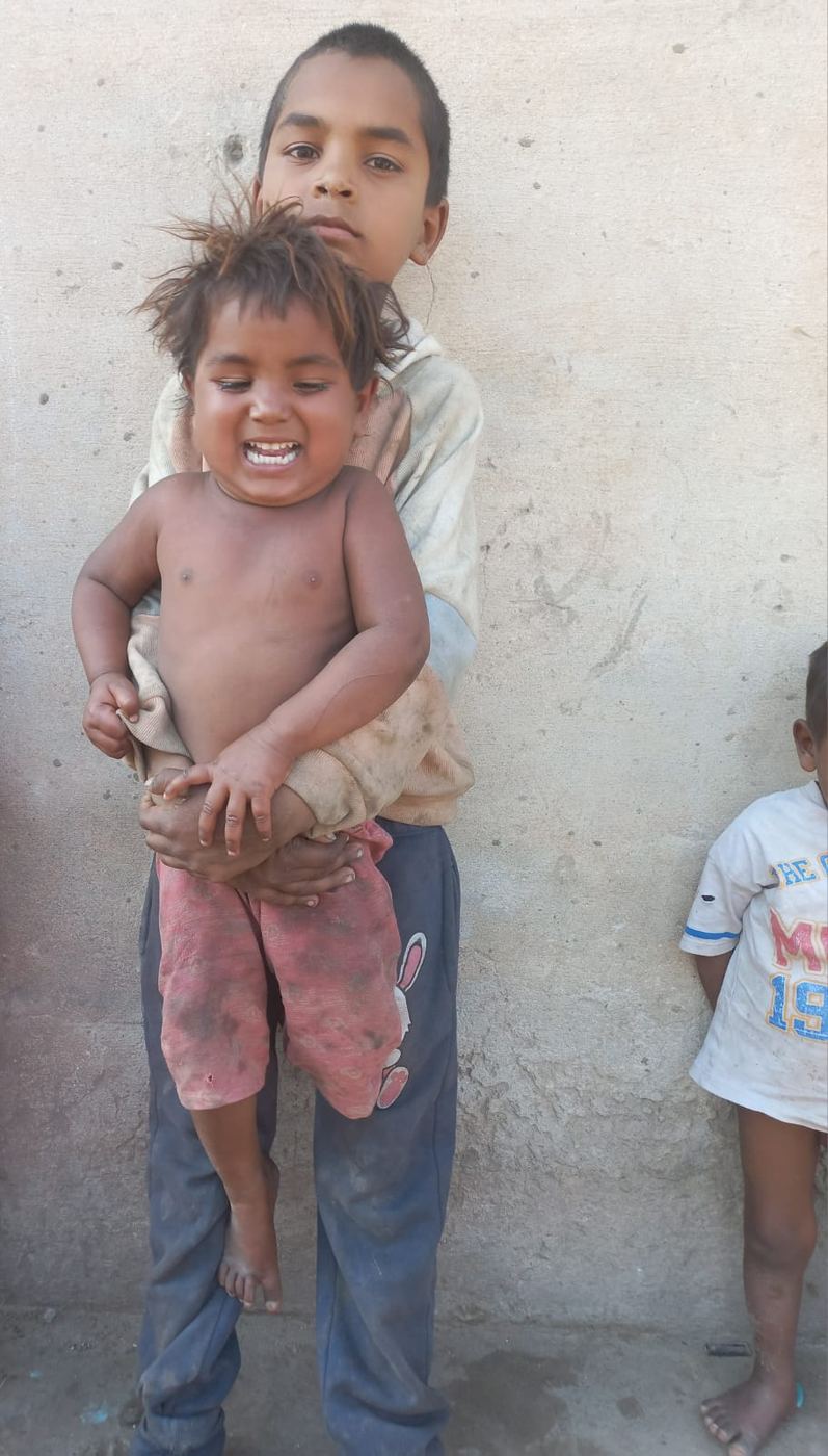 A boy holding his little brother, both dirty and barefoot
