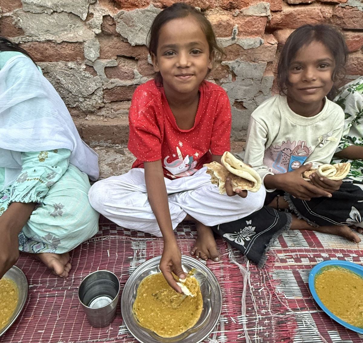 Two smiling girls eating their meal, seated on the ground