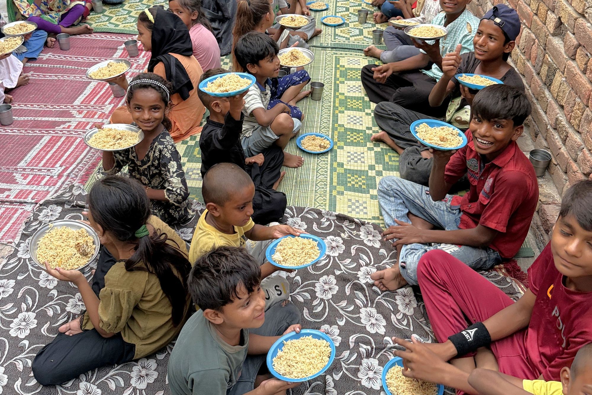 Smiling orphans sitting on the ground holding up their plates of food