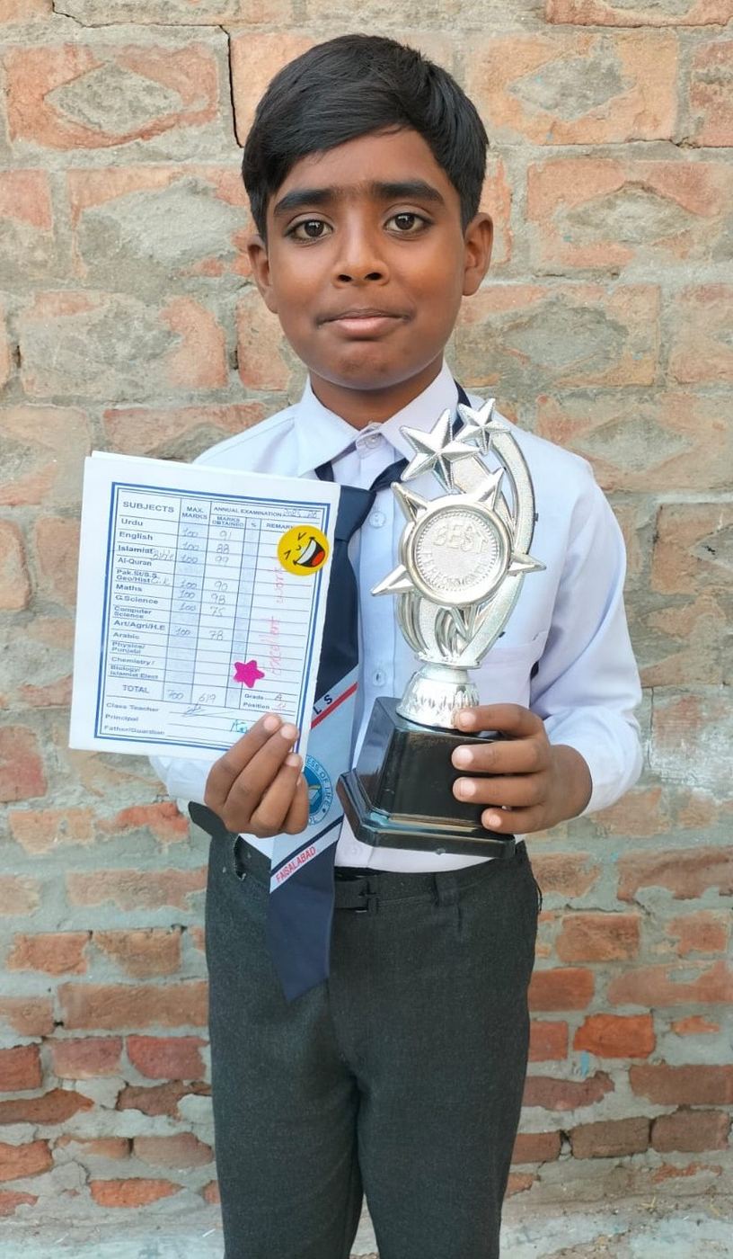 Nehemia in his school uniform, proudly holding his trophy and report card