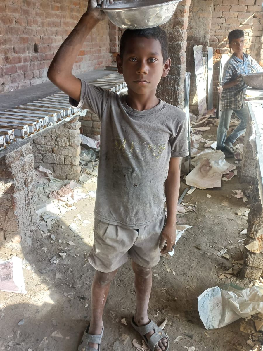 A boy carrying a heavy bowl on his head in a dusty workshop