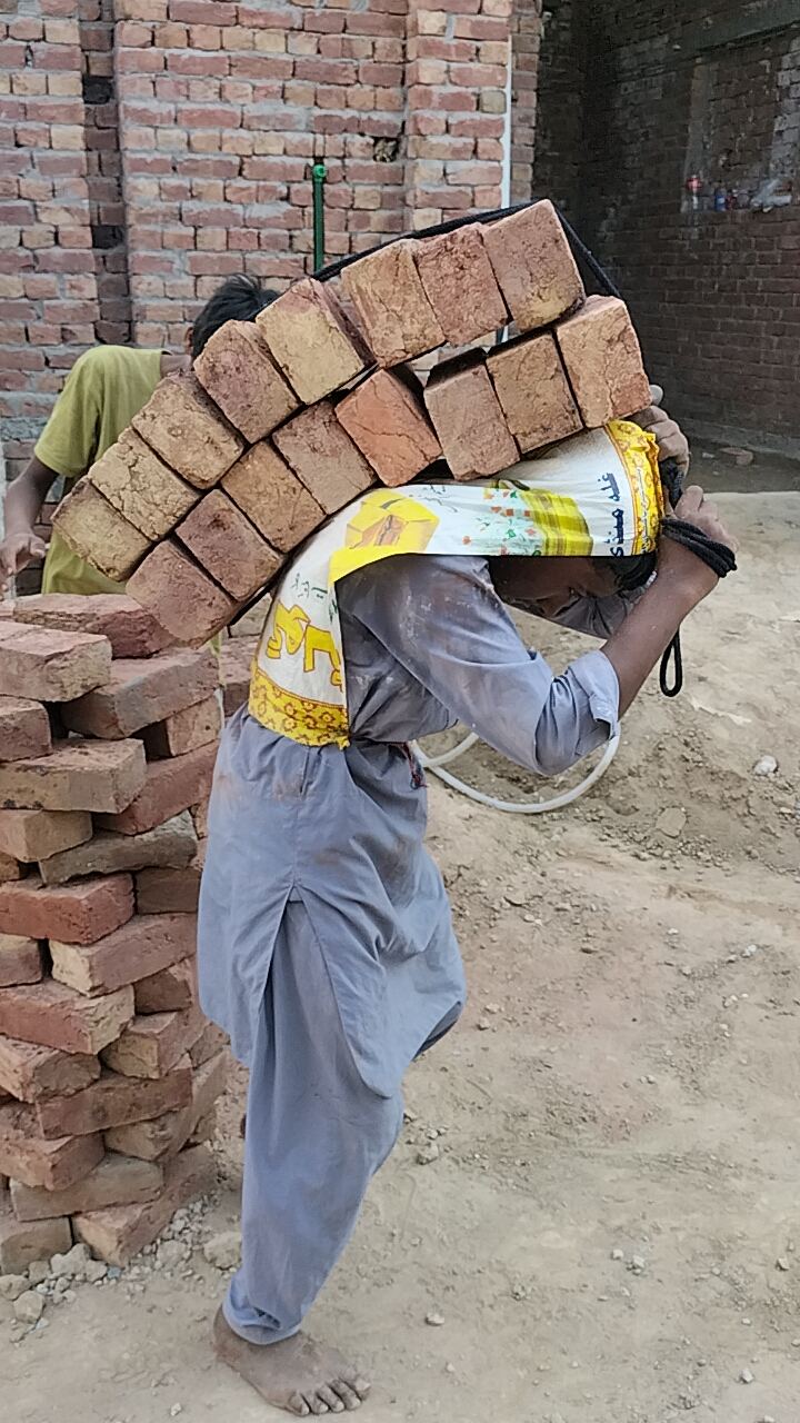 A young barefoot boy carrying a heavy load of bricks on his back
